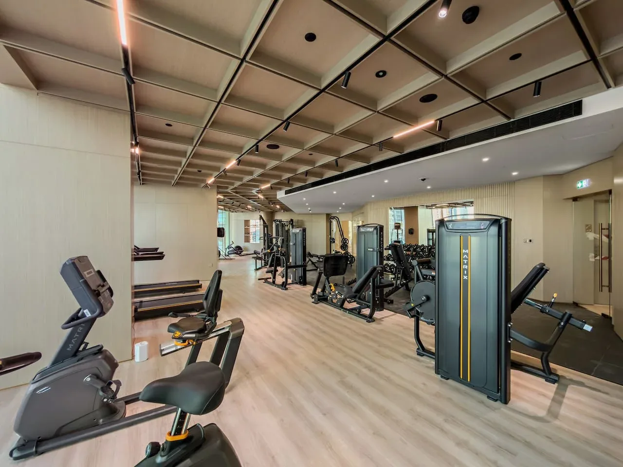 Un gimnasio con máquinas de ejercicio y un amplio suelo de aspecto amaderado.