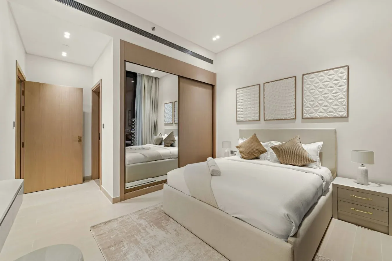 Un dormitorio luminoso con una cama bien tendida y cuadros en la pared.
