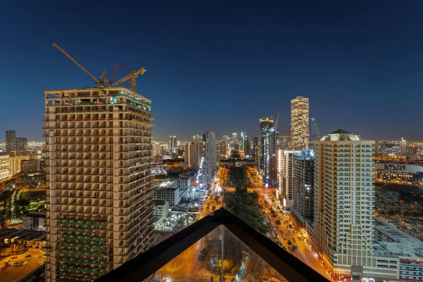 Horizonte urbano nocturno con calles iluminadas y un edificio alto en construcción.