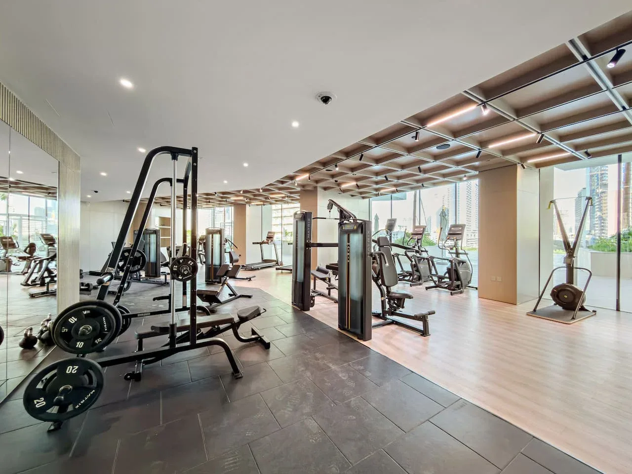 Un gimnasio con máquinas de ejercicio y pesas junto a grandes ventanales.