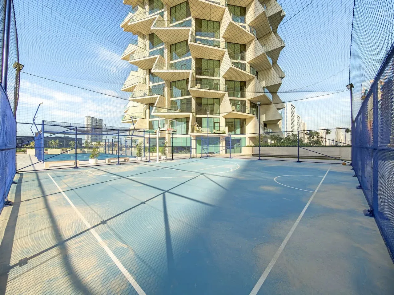 Una cancha al aire libre con cercas azules está frente a un edificio moderno distintivo.