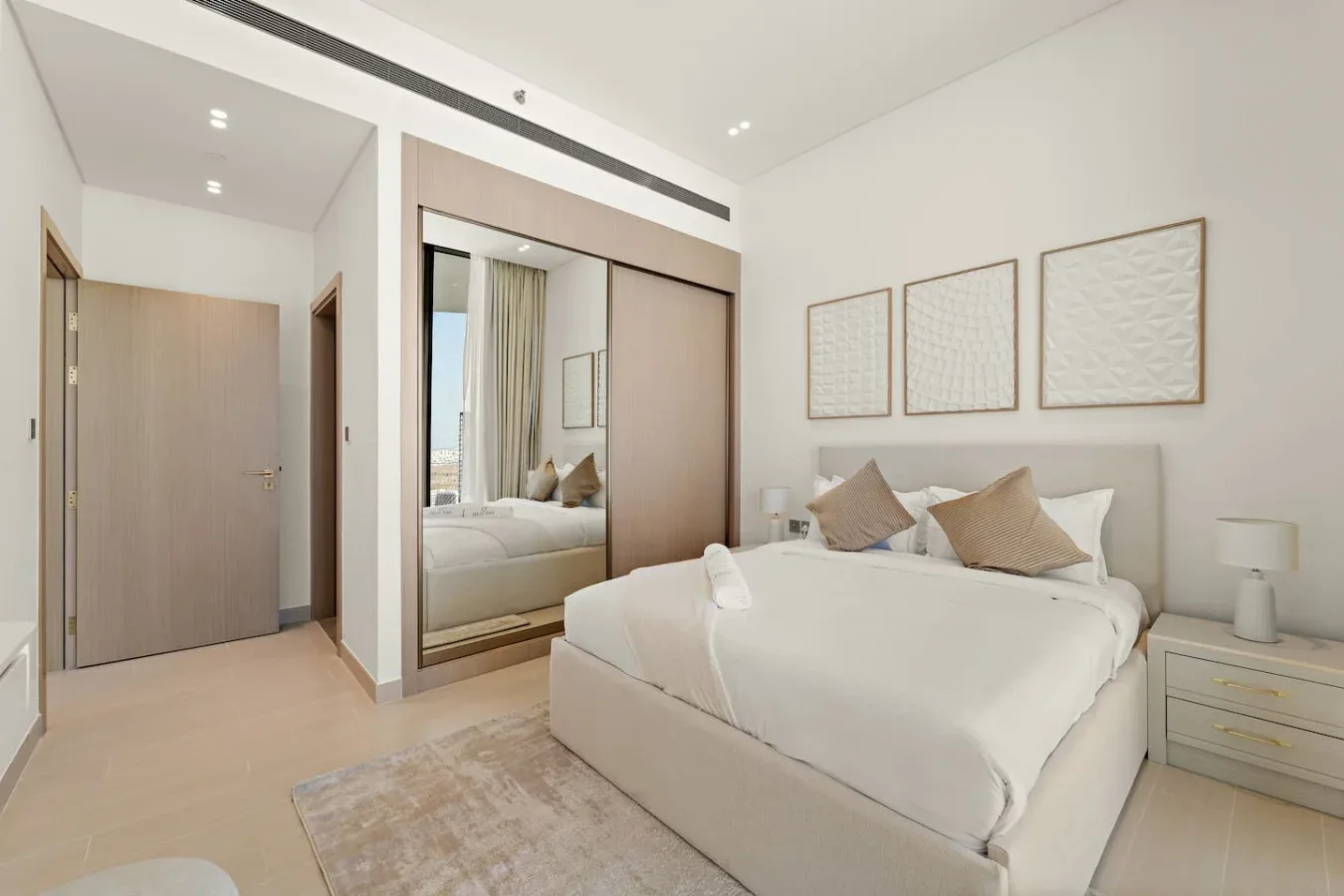 Un dormitorio luminoso con una cama bien tendida y un armario con espejo.