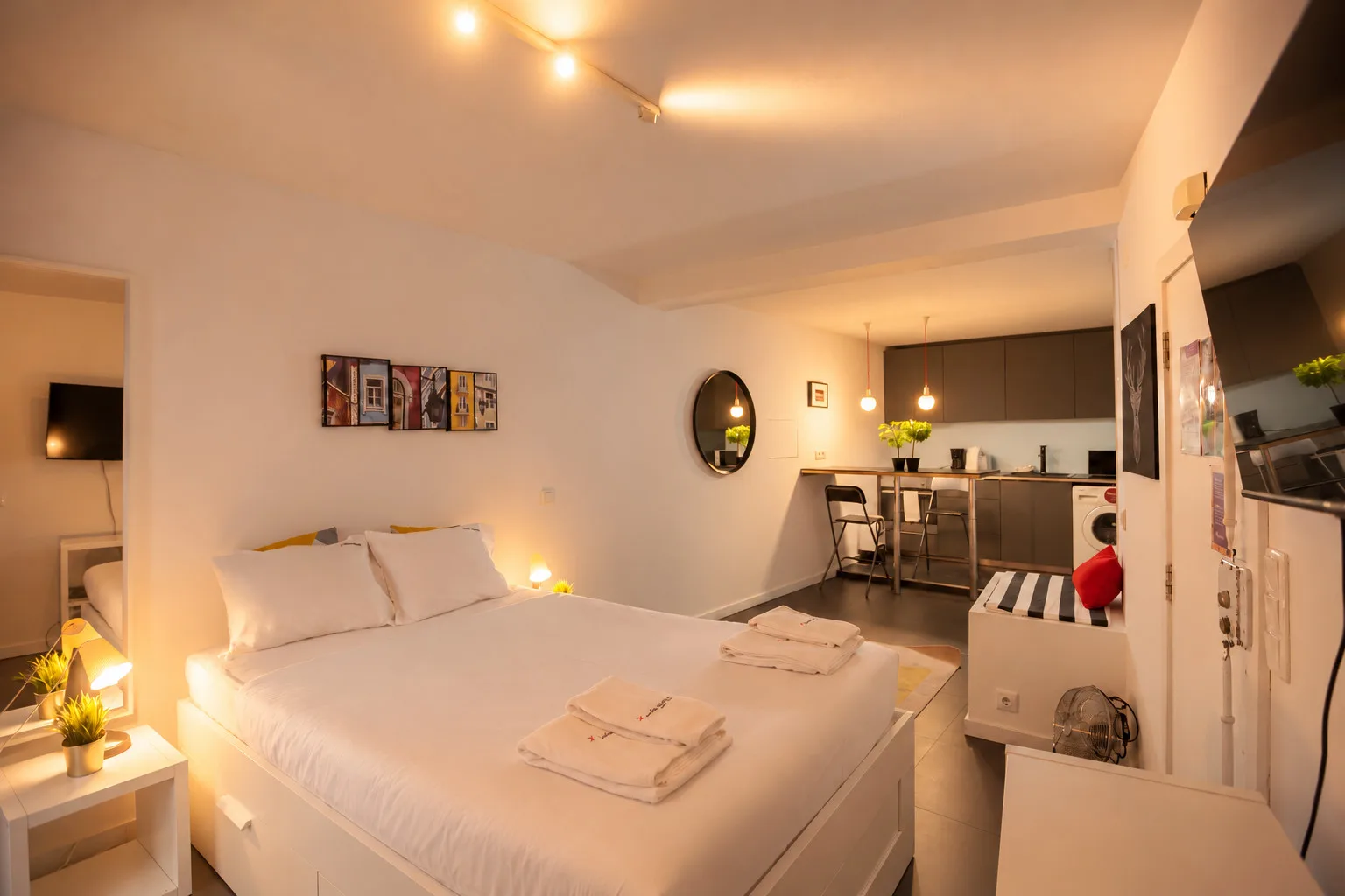 Un dormitorio da a una pequeña cocina, con una cama bien tendida en primer plano.