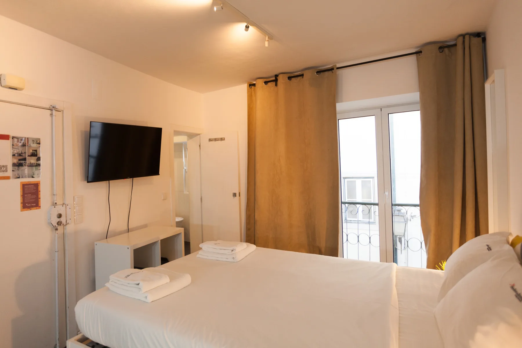 Un dormitorio con una cama bien hecha, un televisor en la pared y puertas acristaladas con cortinas.