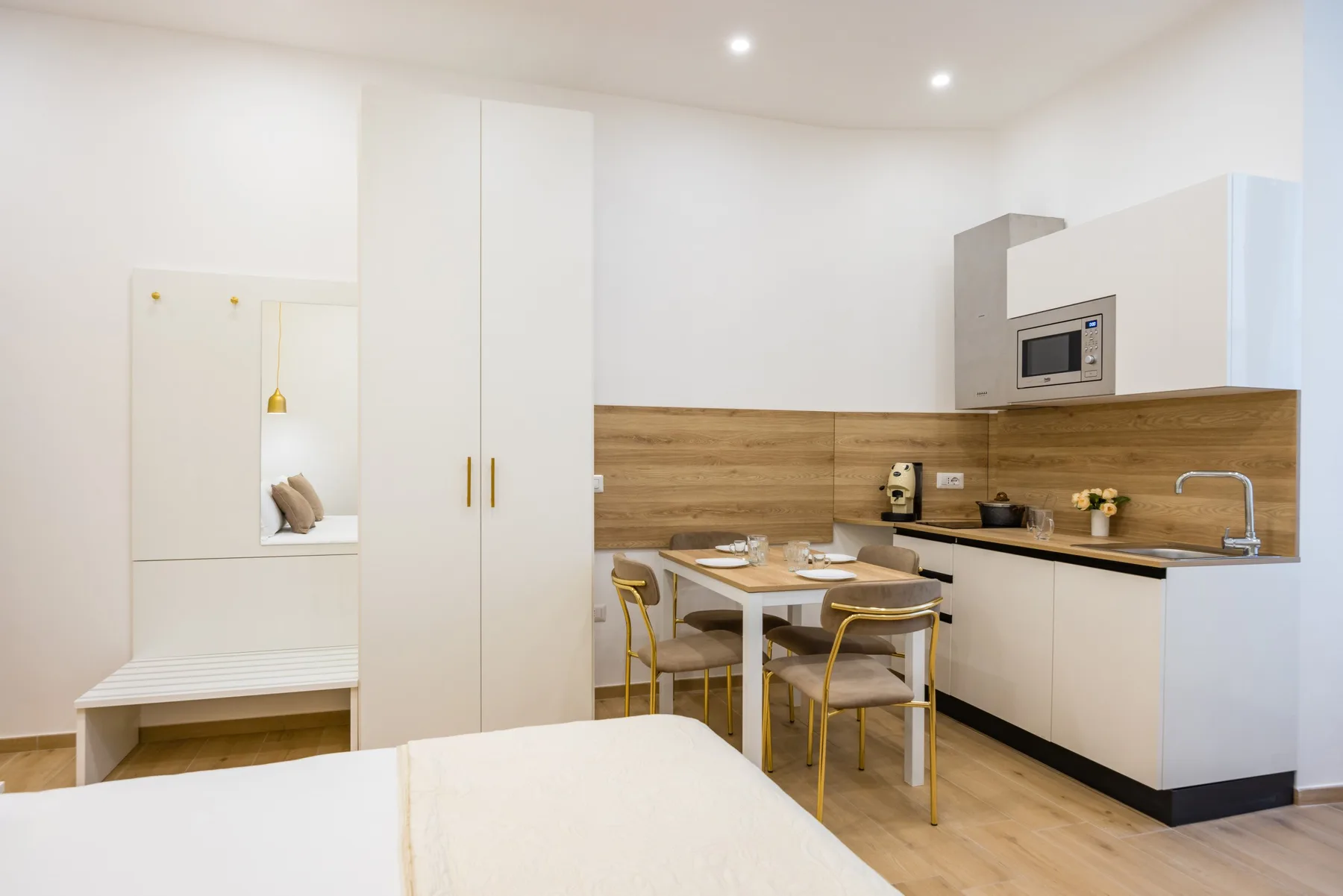 A bright kitchenette with a dining table and built-in storage beside a bed.