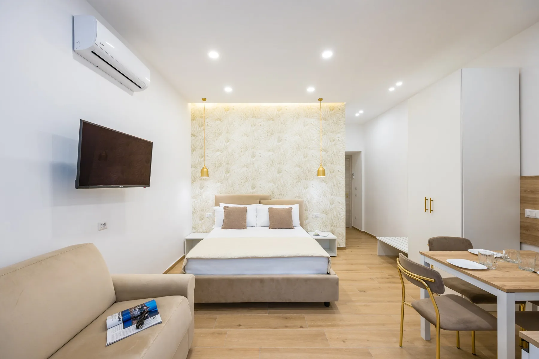 A bright bedroom with a bed, wall-mounted television, and dining table.