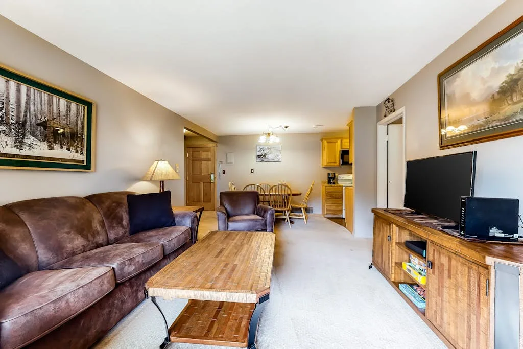 A living room with seating, a coffee table, and a dining area in the background.