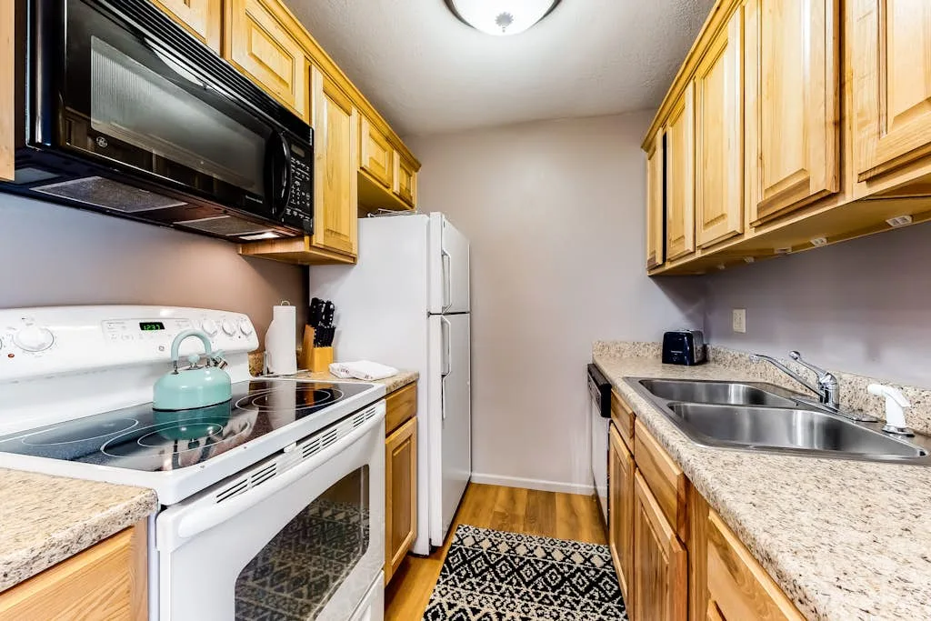 A narrow kitchen with wood cabinets, a stove, and a sink.