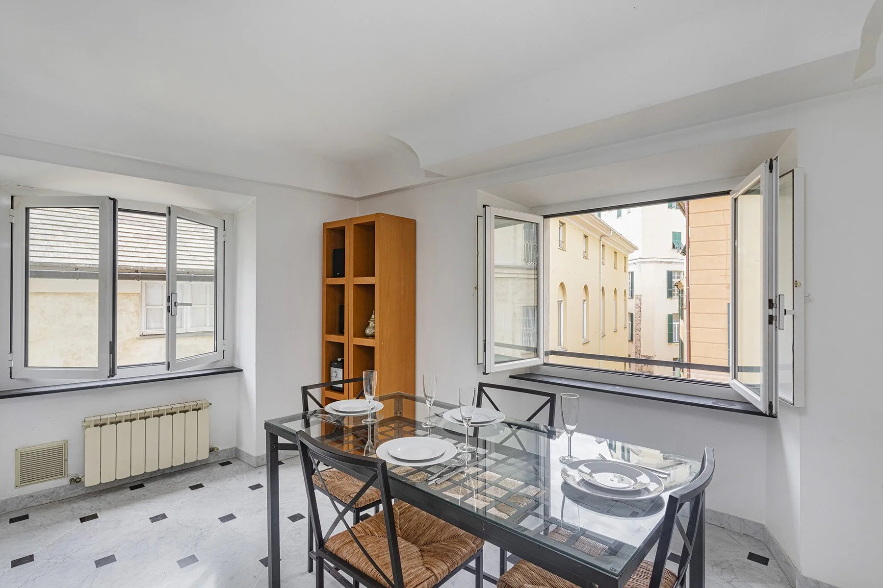 Un comedor con una mesa de vidrio junto a ventanas abiertas.