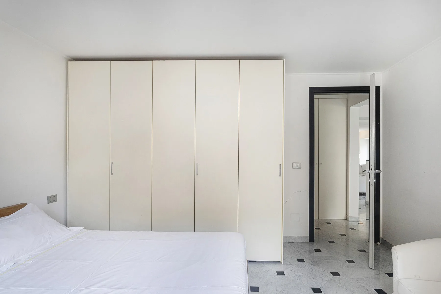 Un dormitorio luminoso con una cama blanca y armarios empotrados.