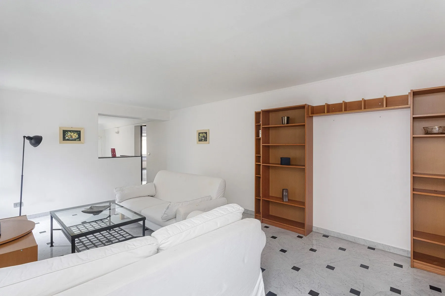 Una sala luminosa con asientos blancos, mesas de vidrio y estanterías empotradas.