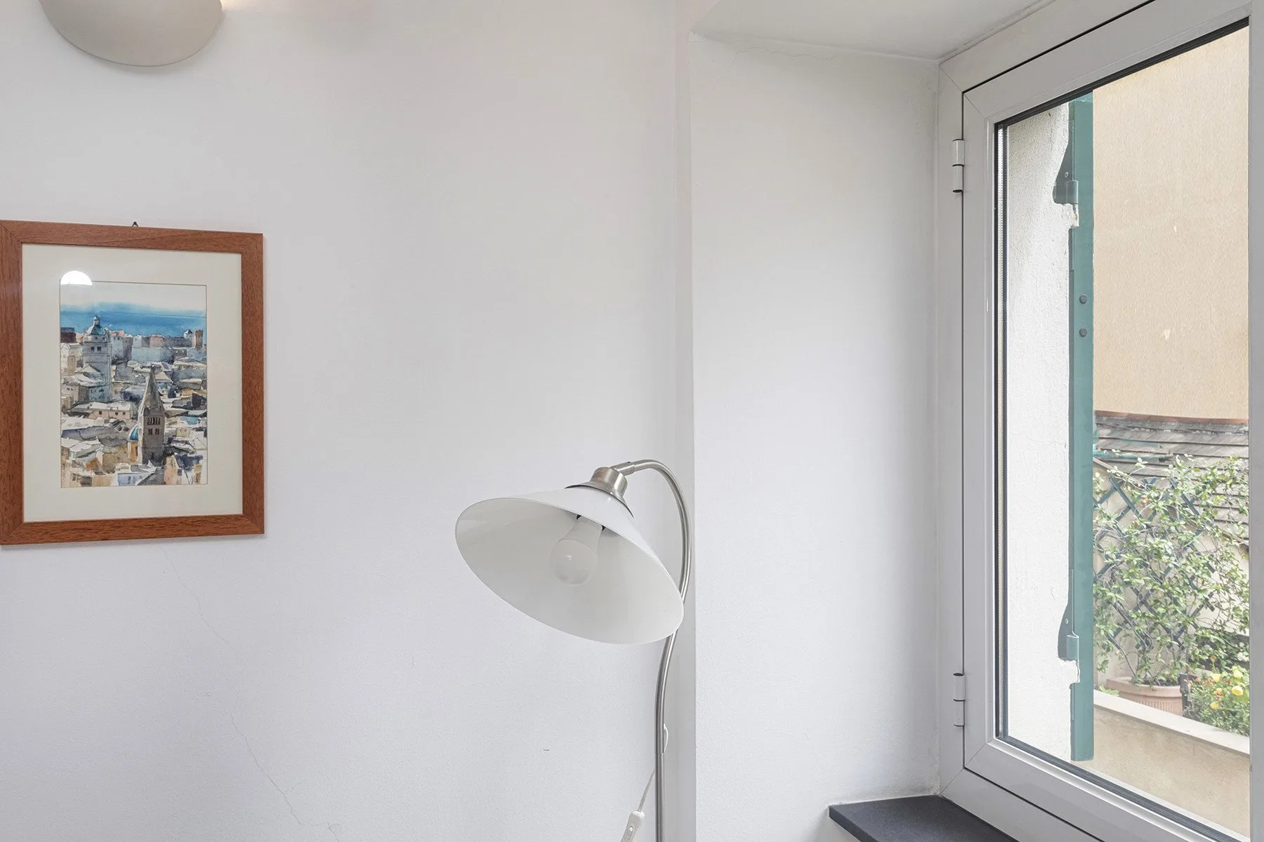 Un rincón luminoso con un cuadro enmarcado, una lámpara de pie y una ventana grande.