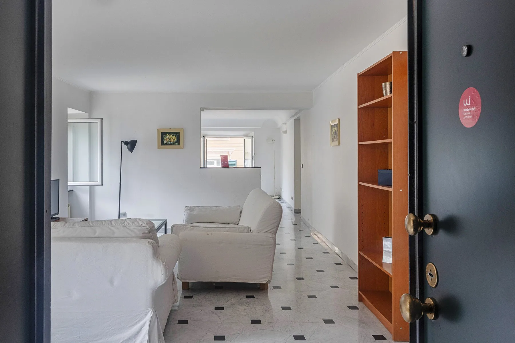 Una sala de estar luminosa con asientos claros y una estantería alta de madera.