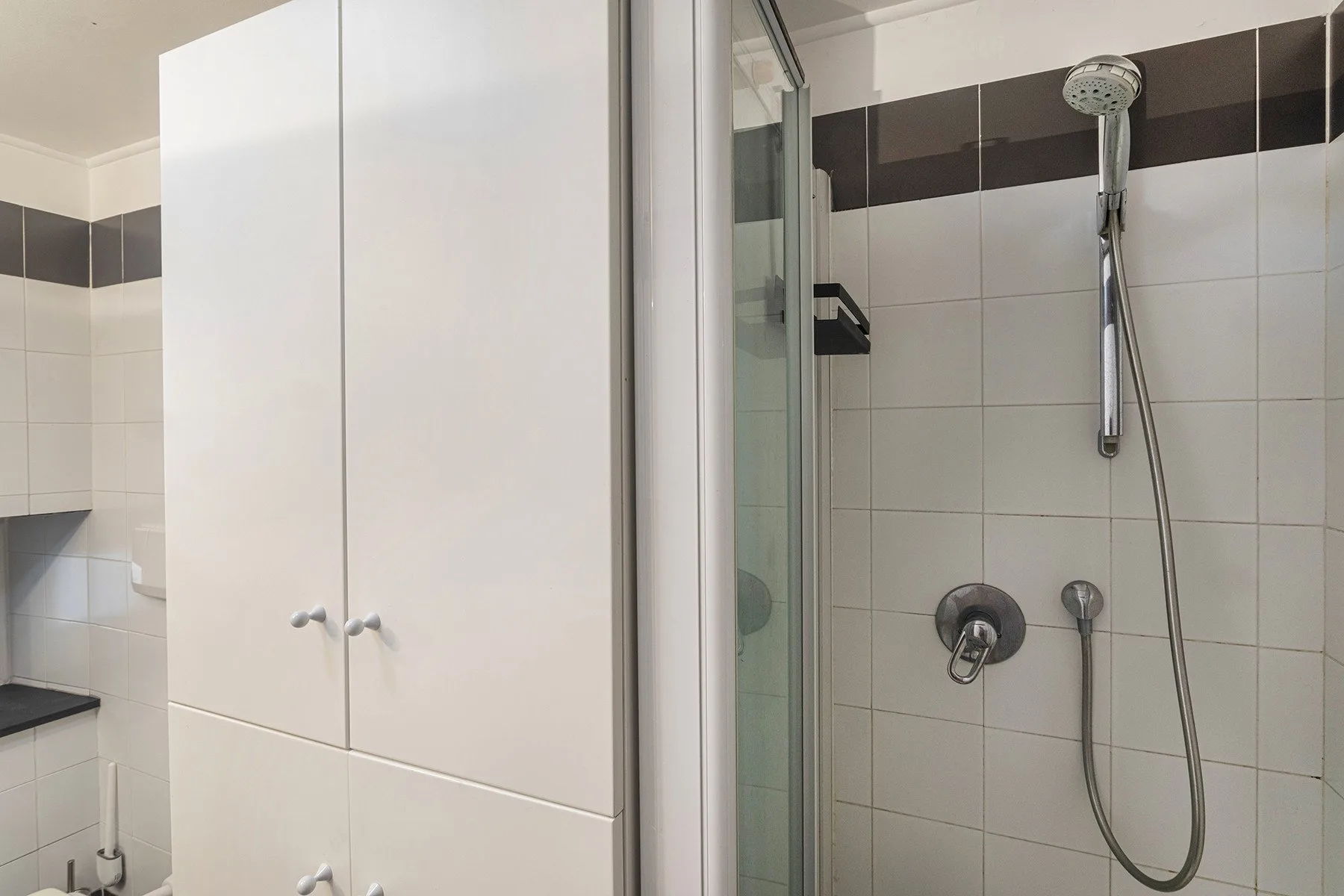 Un baño alicatado con ducha de pared y armarios blancos.