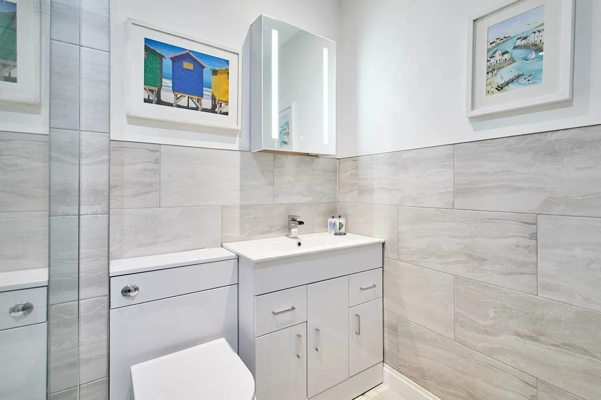 A bright bathroom with a white vanity and framed coastal artwork.