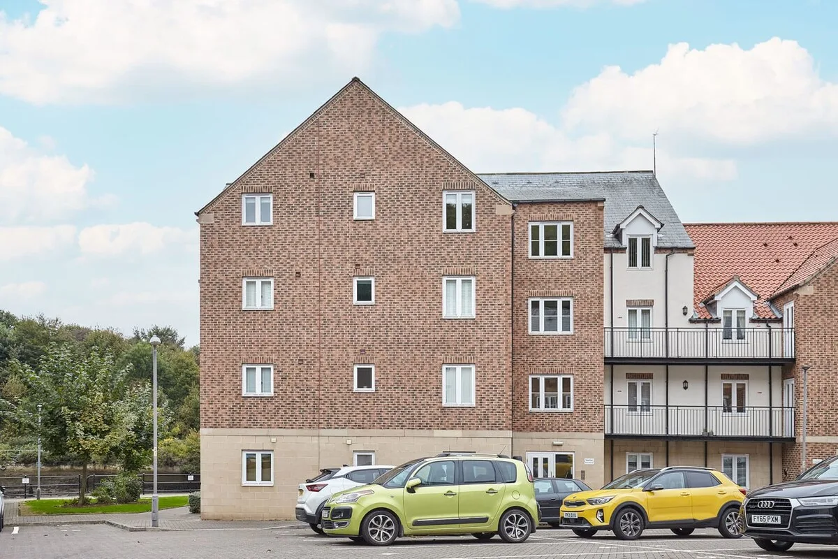 A brick residential building stands behind several parked cars.