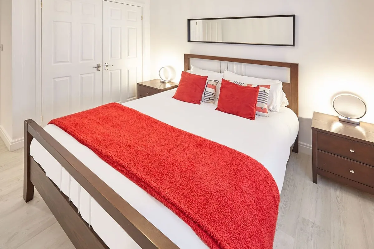 A bedroom with a bed dressed in white and red bedding.