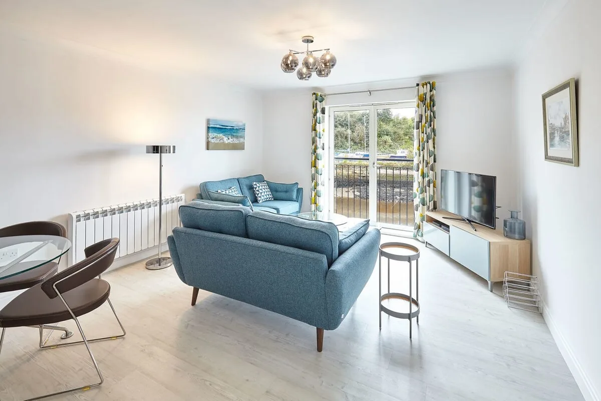 A bright living room with blue seating and glass doors opening onto a balcony.