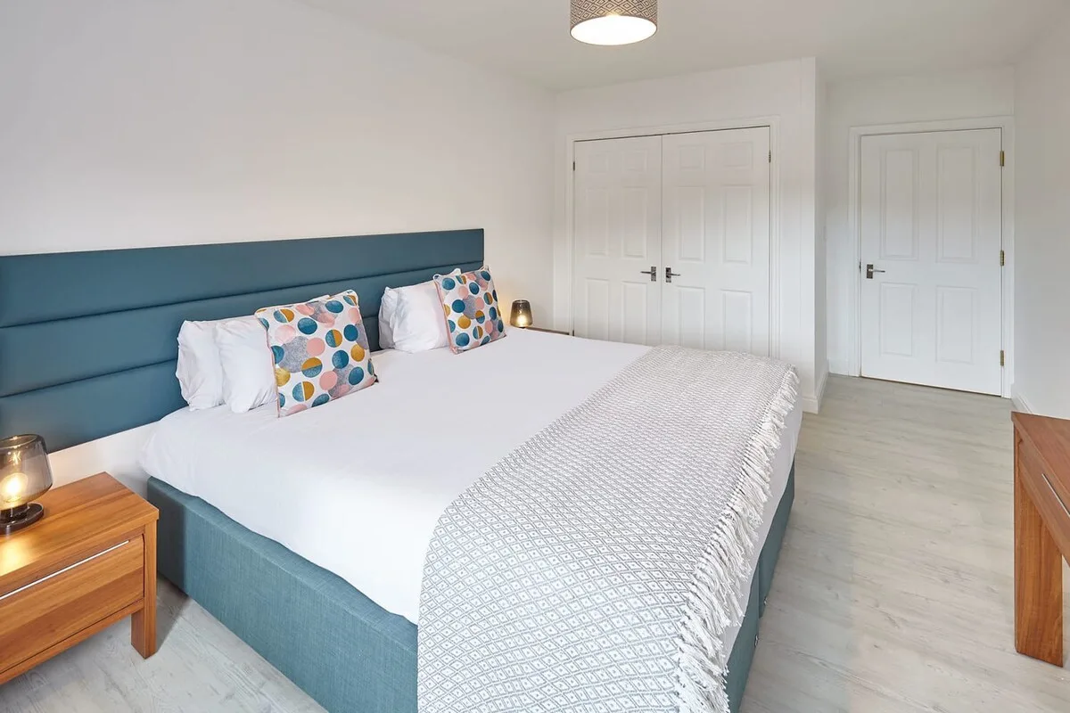 A bedroom with a large bed, patterned pillows, and white closet doors.