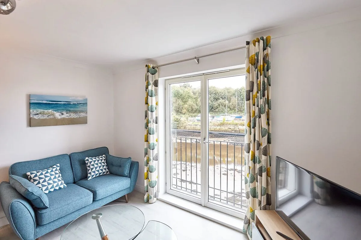 A bright living room with blue seating beside glass doors opening onto a balcony.