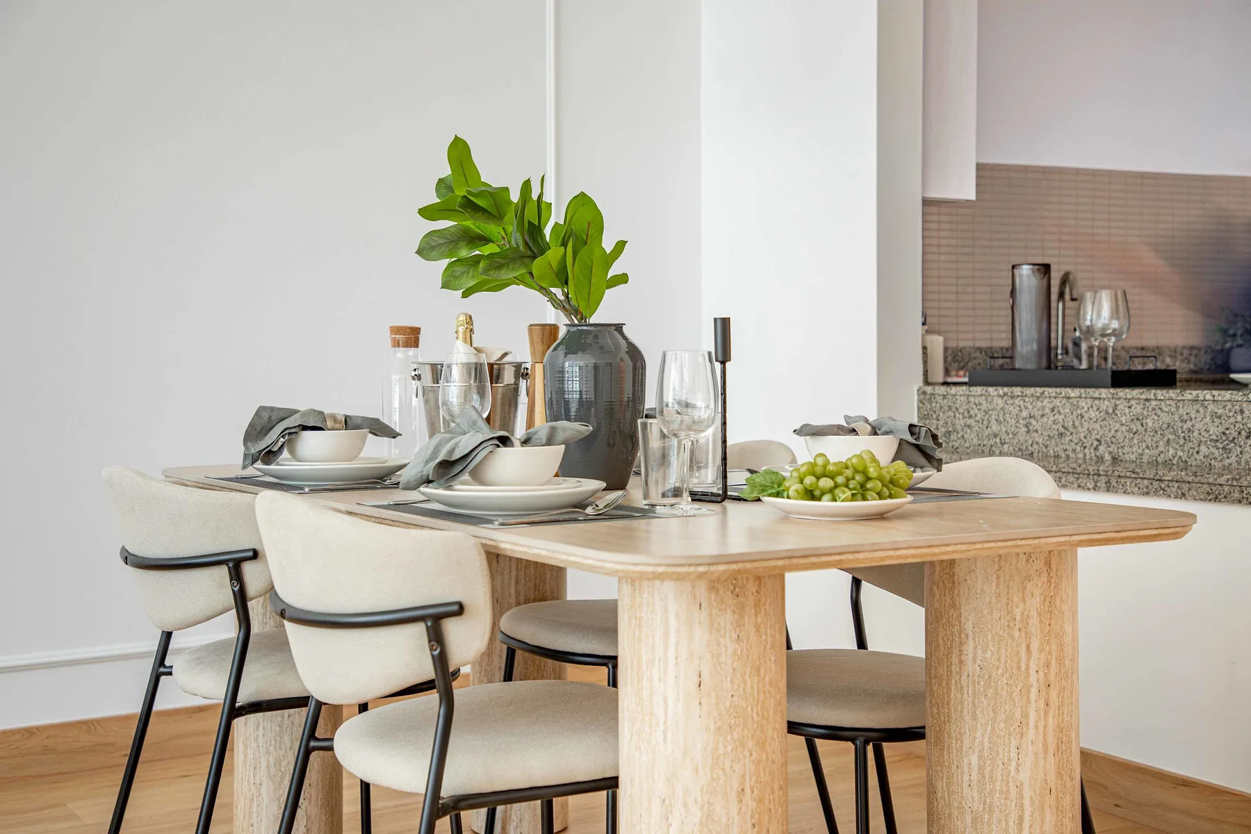 Comedor con una mesa puesta, asientos acolchados y un centro de mesa con hojas.