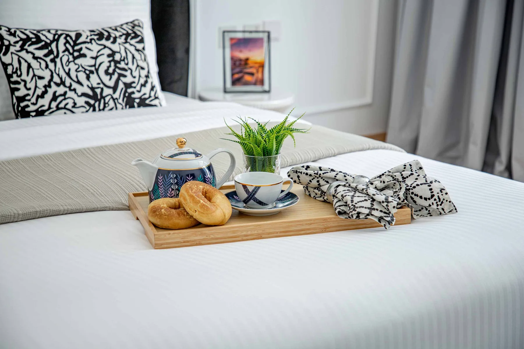 Una cama bien tendida con una bandeja que contiene té, bollería y una planta pequeña.