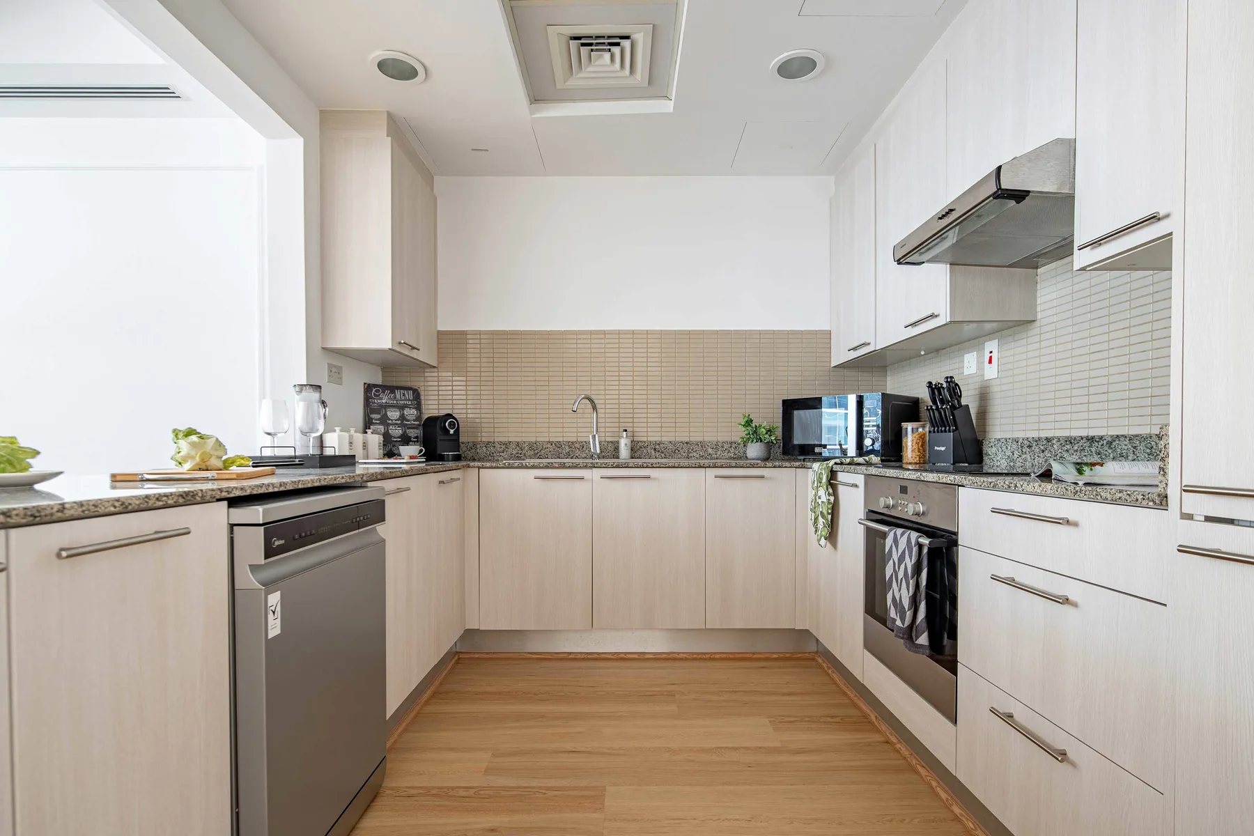 Una cocina moderna con gabinetes claros, electrodomésticos sobre la encimera y suelo de tono madera.