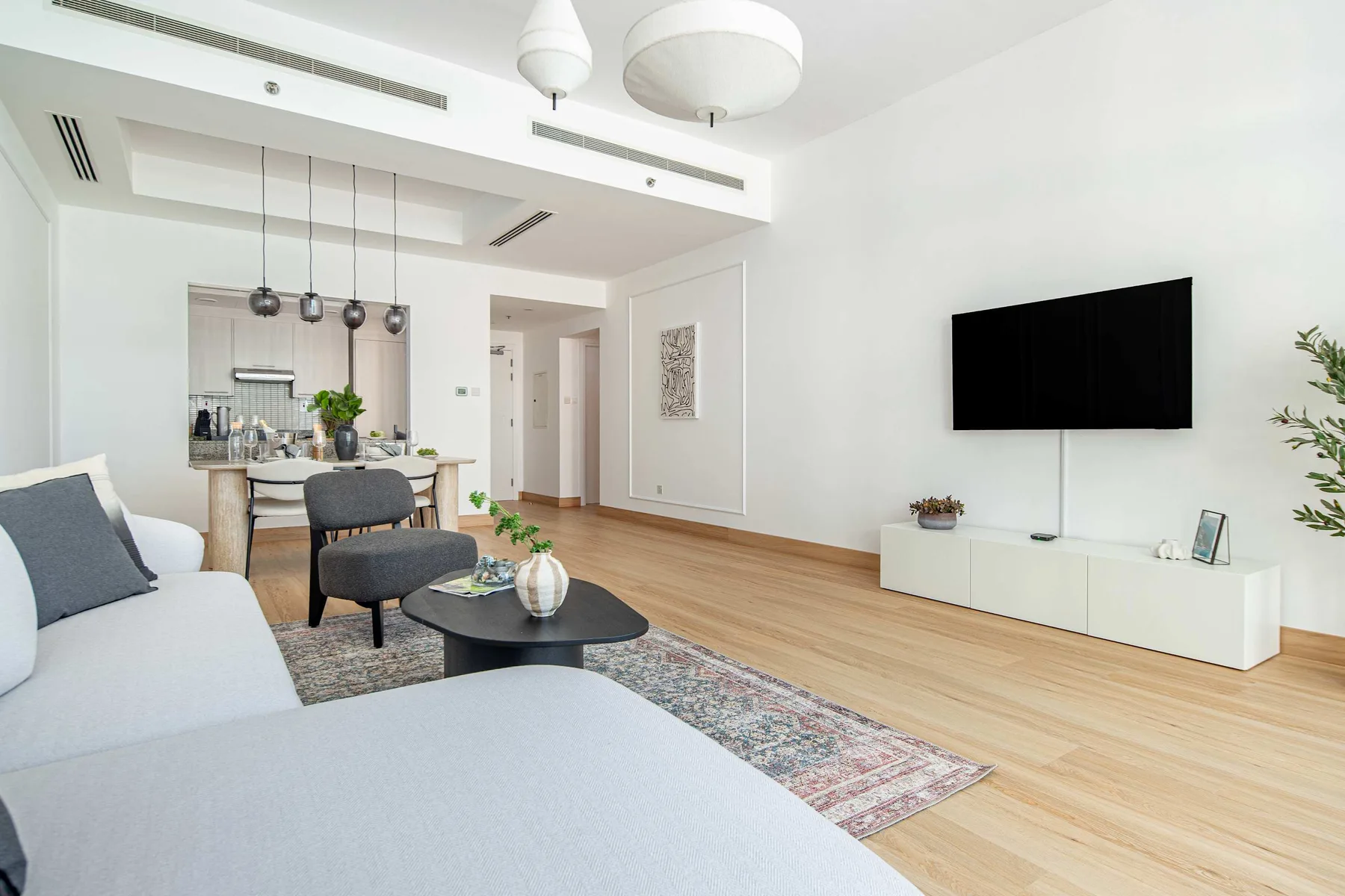 Una sala de estar luminosa con asientos, una mesa de centro y un televisor en la pared.