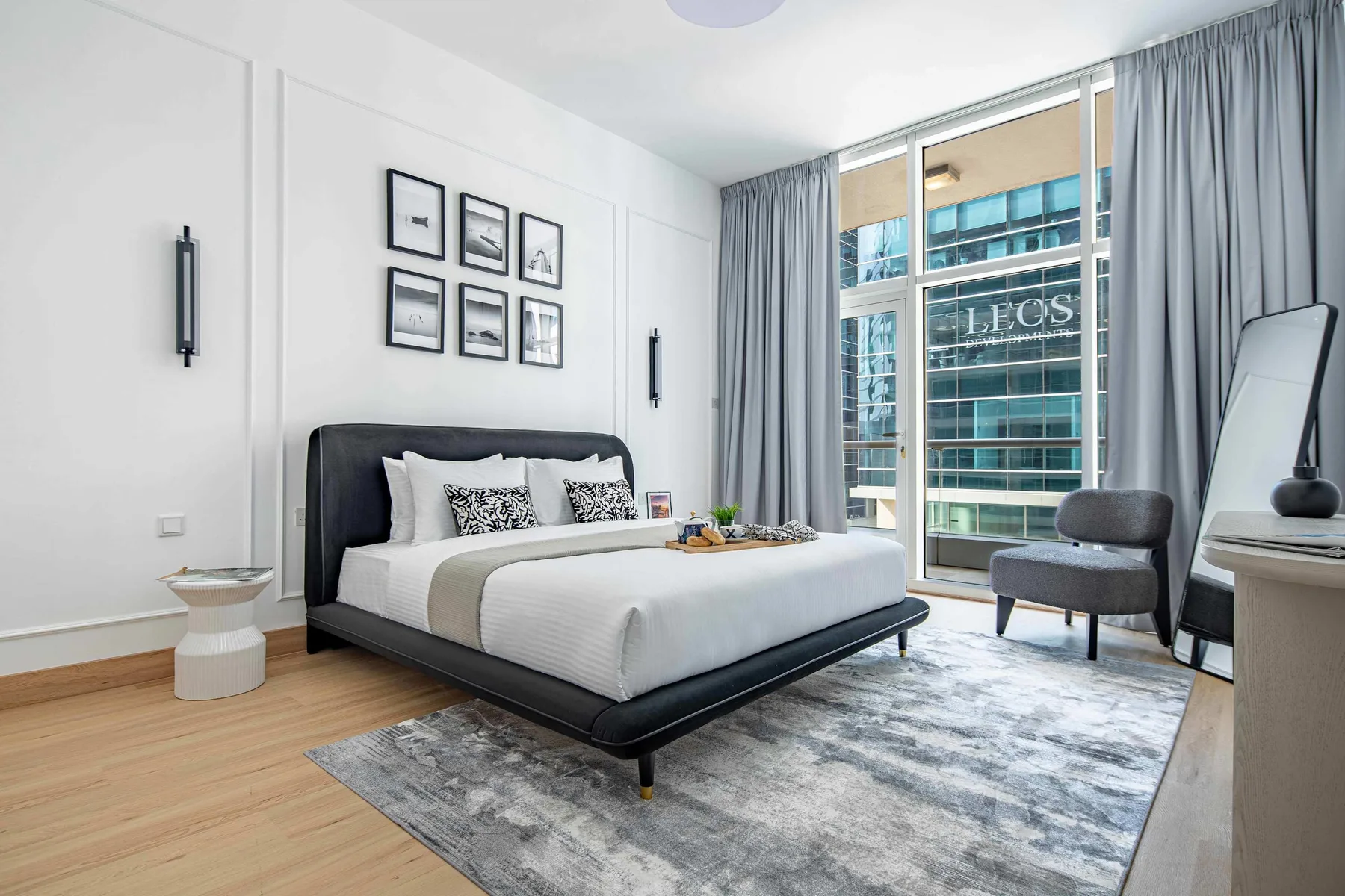 Un dormitorio luminoso con una cama, cuadros enmarcados y grandes ventanas.