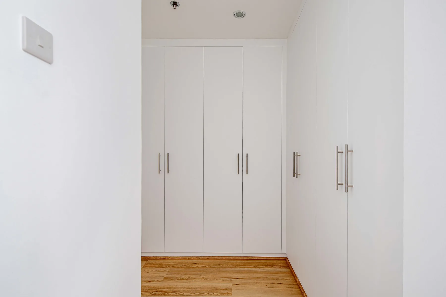 Un pasillo blanco con armarios empotrados y suelo de madera.