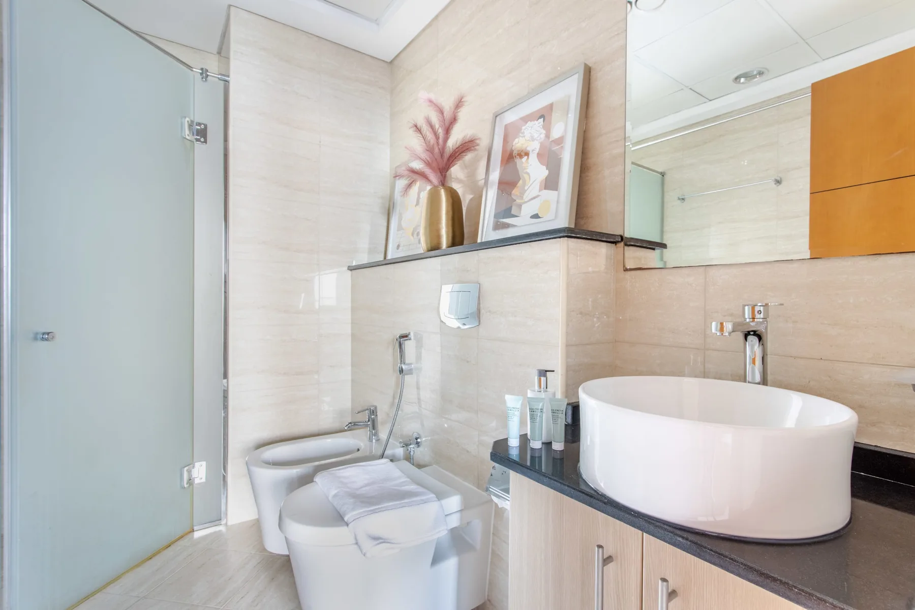 Un baño luminoso con azulejos, ducha de vidrio, inodoro y lavabo sobre encimera.