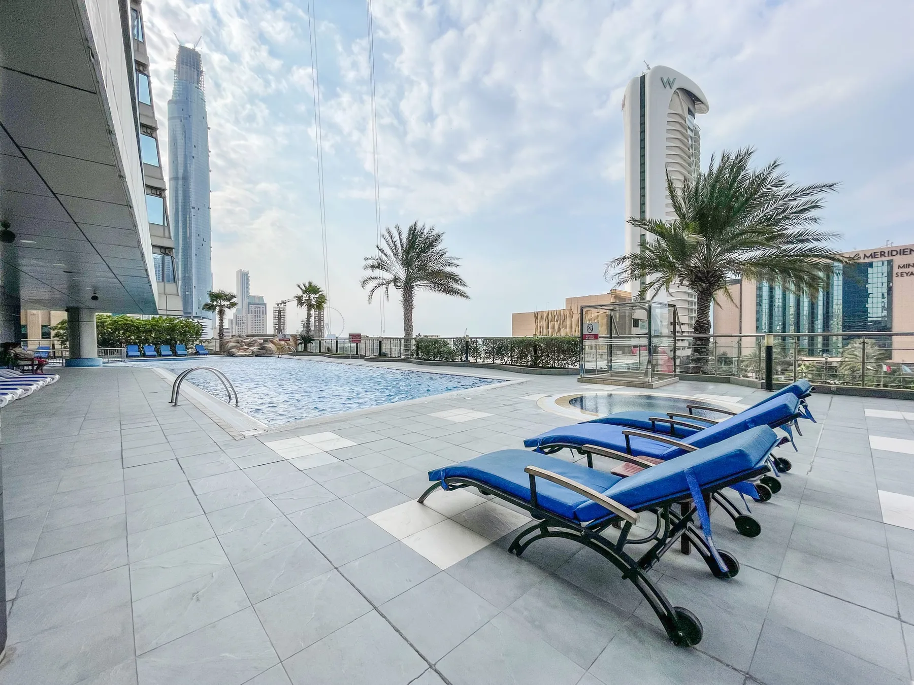 Una piscina en la azotea con tumbonas azules y edificios de la ciudad al fondo.
