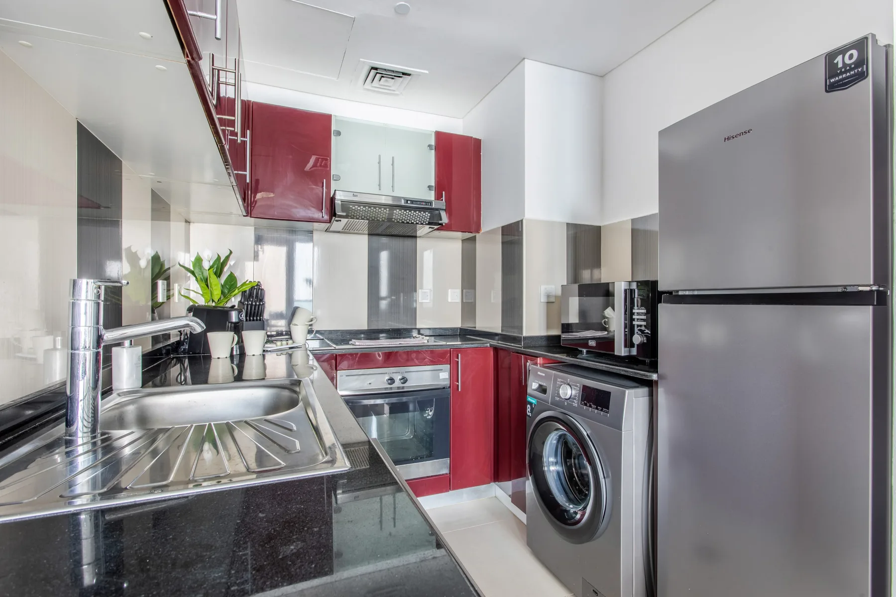 Una cocina compacta con armarios rojos, electrodomésticos de acero inoxidable y un fregadero.