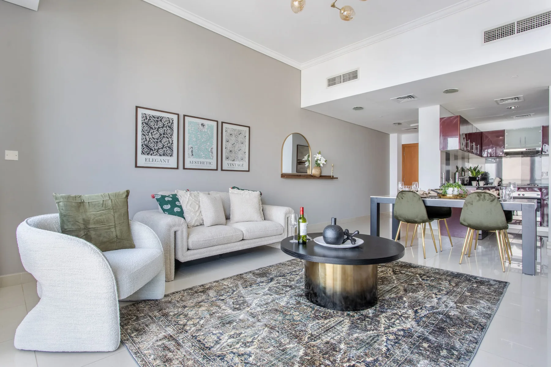 A bright living room with seating around a round coffee table, opening onto a kitchen.