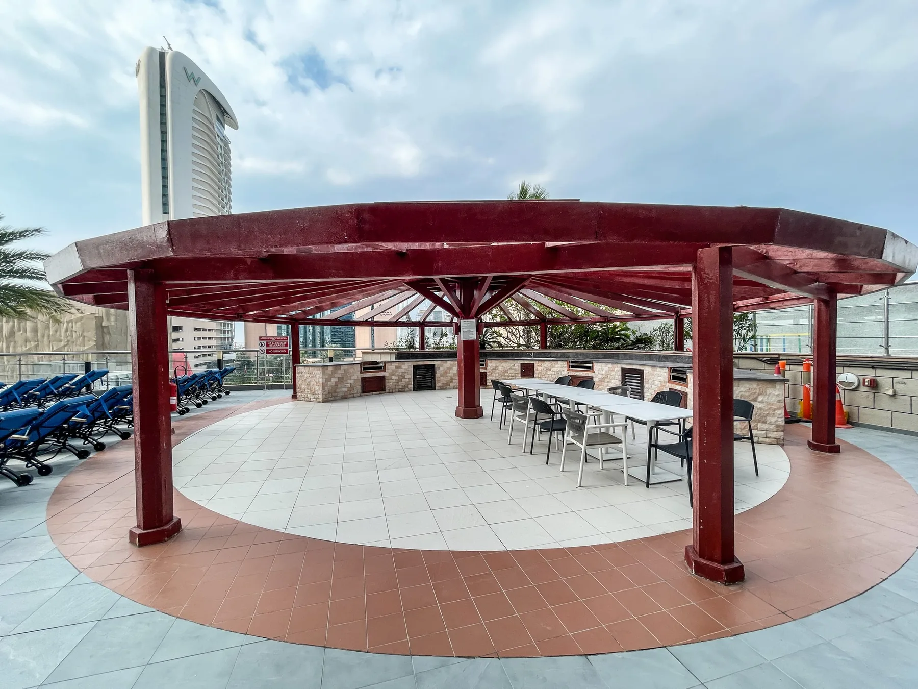 Un patio exterior cubierto tiene una zona circular embaldosada con mesas y asientos.