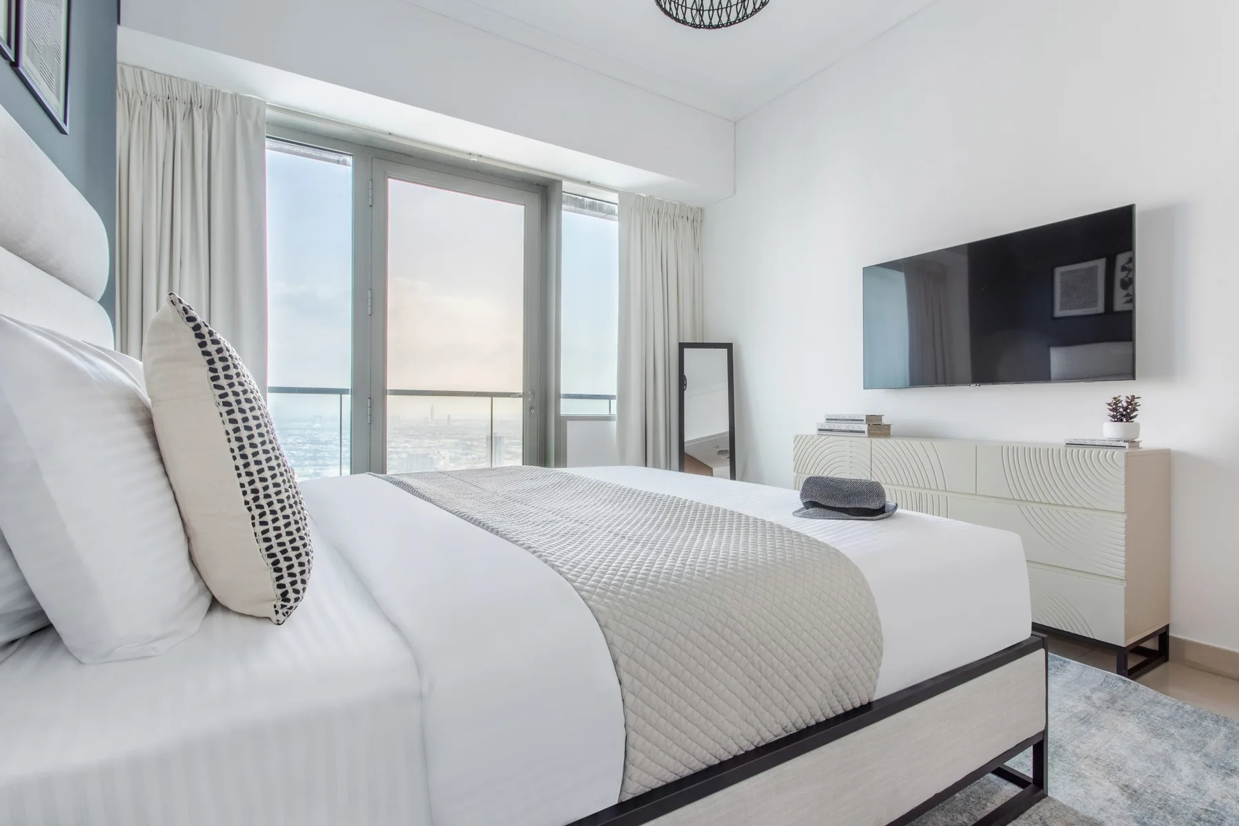 Un dormitorio luminoso con una cama bien tendida y un televisor en la pared.