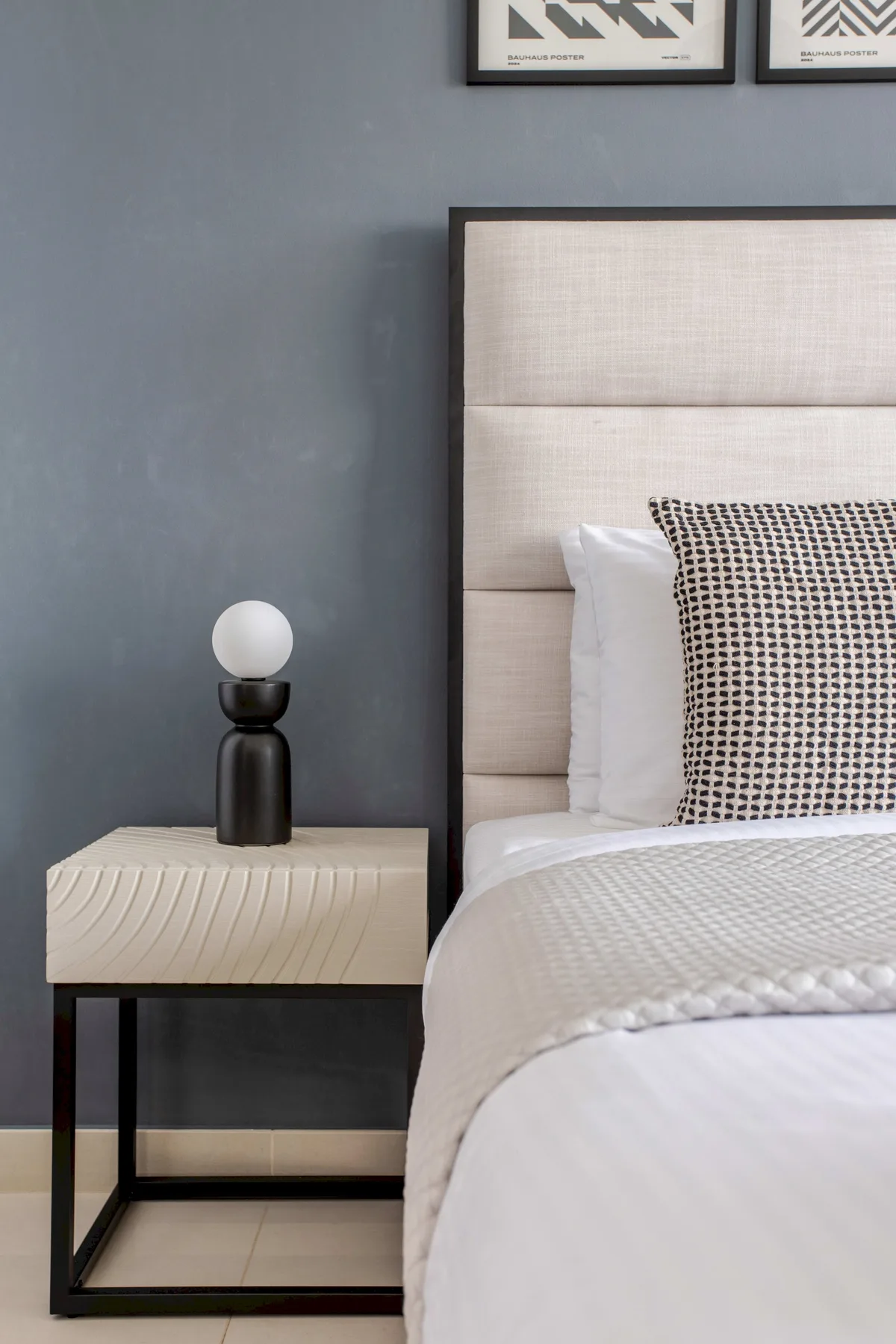 Un dormitorio con una cama tendida junto a una mesita de noche y una lámpara.