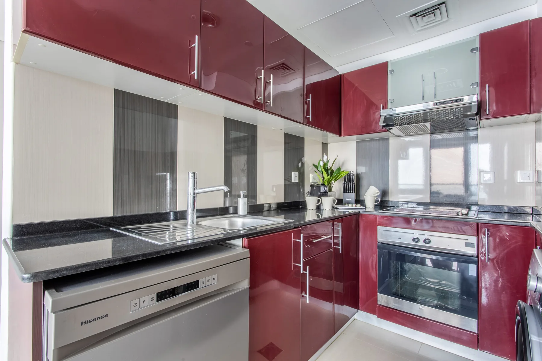 Una cocina moderna con gabinetes rojo oscuro, una placa de cocción y un horno.
