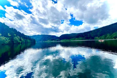 A calm lake reflects a cloudy sky, with forested hills along the shore.