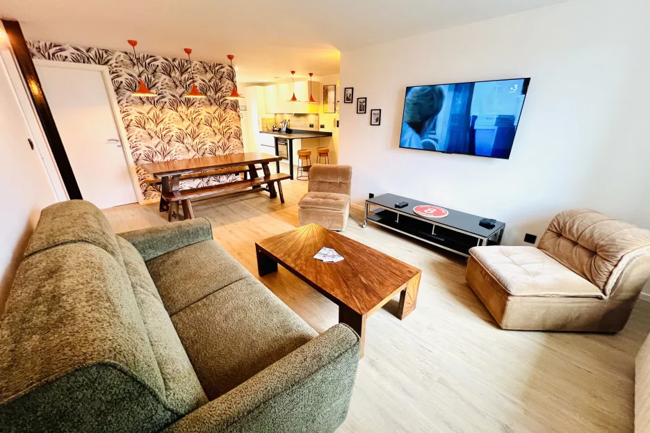 A bright living room with seating, a wooden coffee table, and a wall-mounted television.