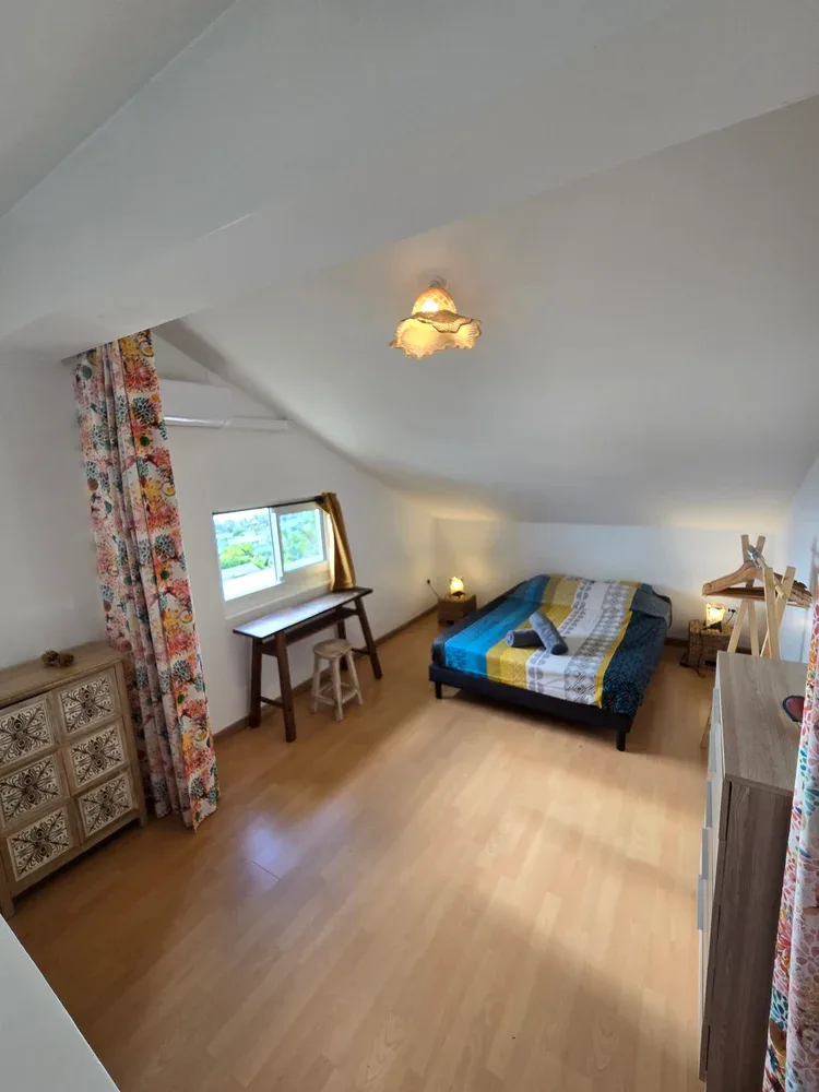 A sloped-ceiling bedroom with a bed, desk, and window.