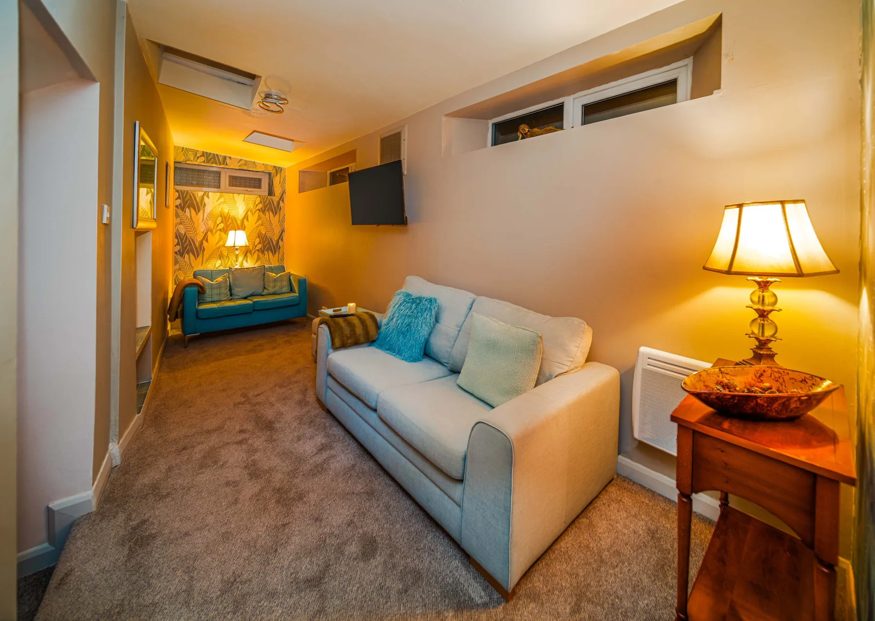 A narrow living room with a sofa, a lamp, and a television.