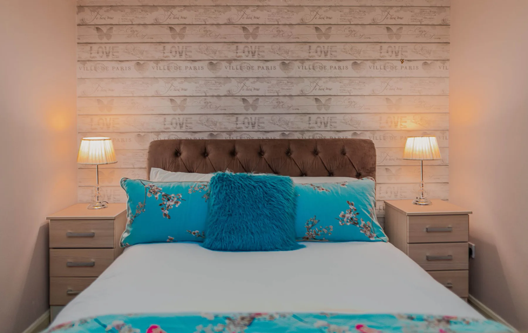 A bedroom with a neatly made bed, turquoise pillows, and matching bedside lamps.
