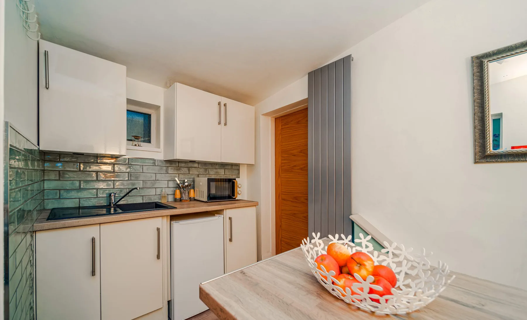 A compact kitchen with white cabinets, a dark countertop, and a fruit bowl.