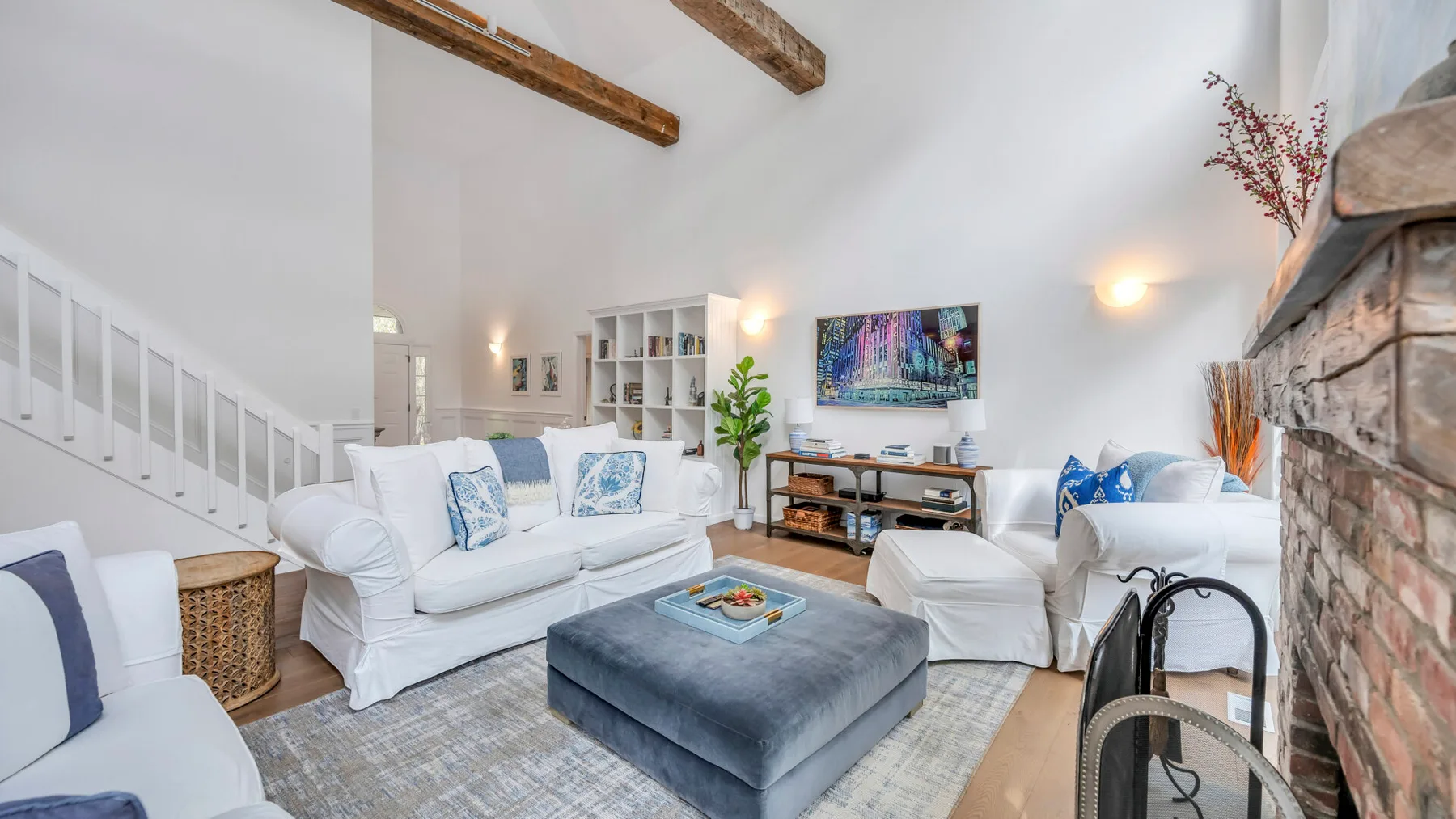 Una sala luminosa con asientos blancos, un otomano grande y un televisor.