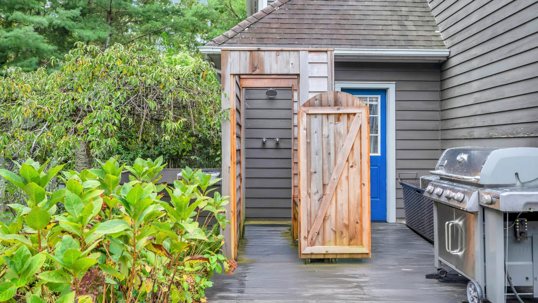 Una pequeña zona exterior para cambiarse, con una puerta de madera abierta junto a una terraza.