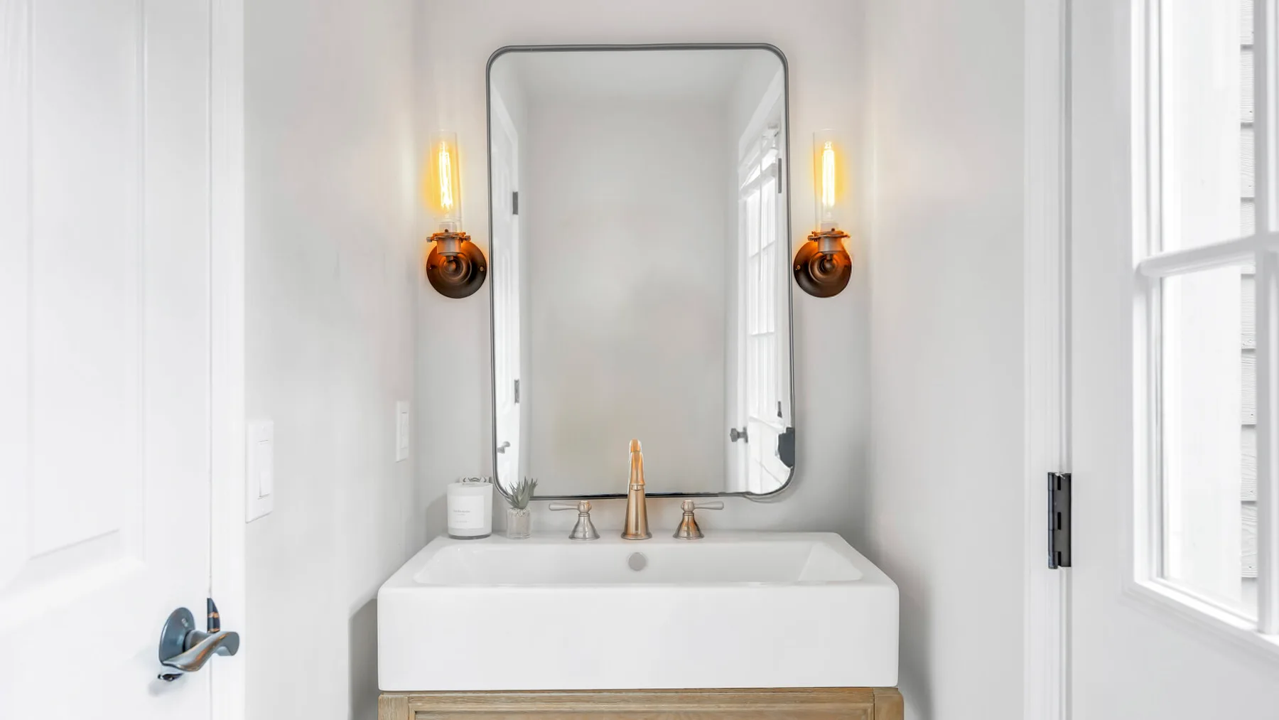 Un lavabo de baño luminoso con un espejo de pared y dos apliques encendidos.