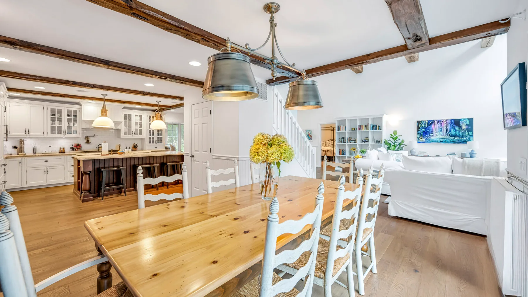Un espacio abierto de comedor y sala de estar cuenta con una mesa de madera y asientos blancos.