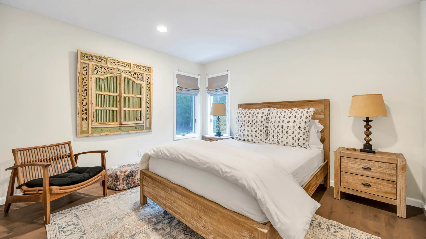 Un dormitorio con una cama de madera, cojines estampados y una silla junto a la ventana.