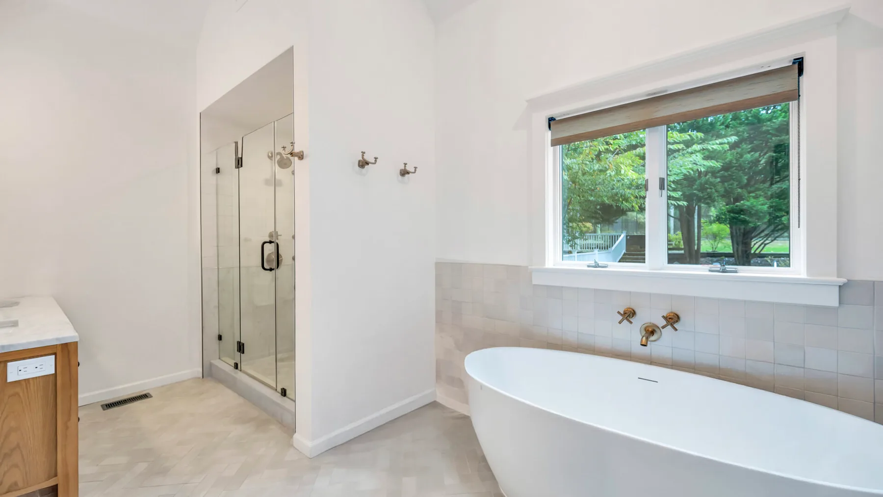 Un baño luminoso con bañera exenta, ducha de vidrio y una ventana con vistas a la vegetación.